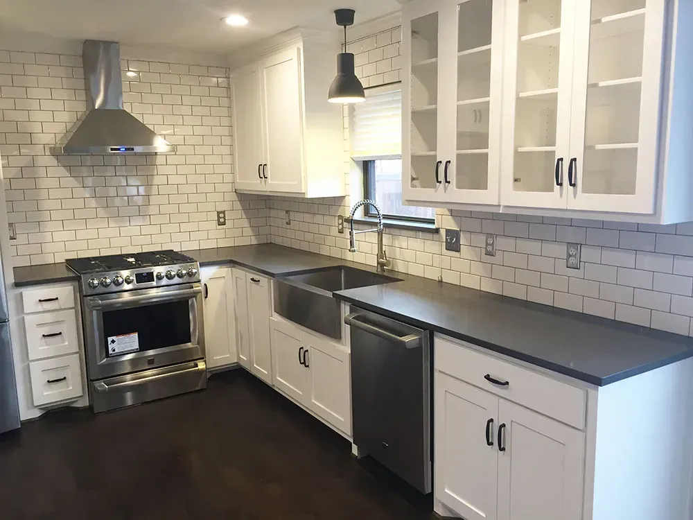 White kitchen with stainless steel appliances, dark countertops, and brick-patterned backsplash.