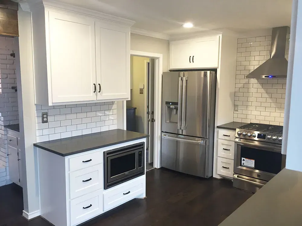 White kitchen with dark countertops, stainless steel appliances, and subway tile backsplash.