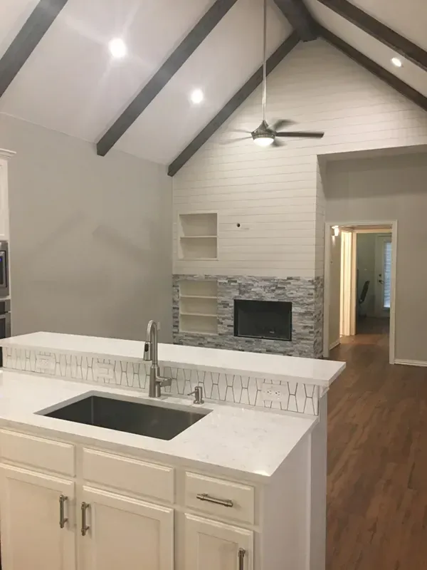 Kitchen with island, fireplace, and high ceilings with dark beams. White cabinets, gray walls, and wooden floors.