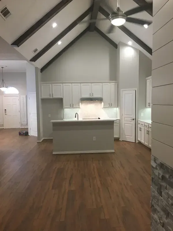 Kitchen with high ceiling, light cabinets, island, wood floor, and exposed beams.