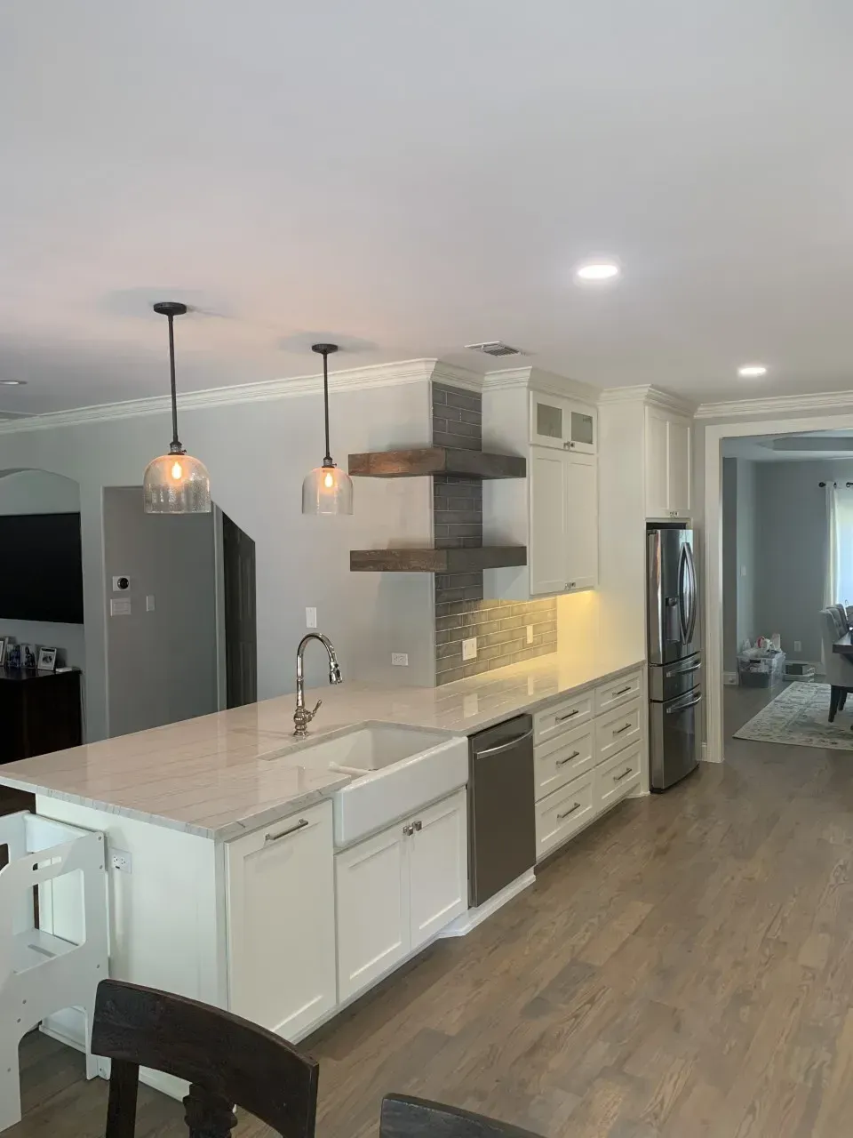 Modern kitchen with white cabinets, island, stainless steel appliances, pendant lights, and wooden shelves.