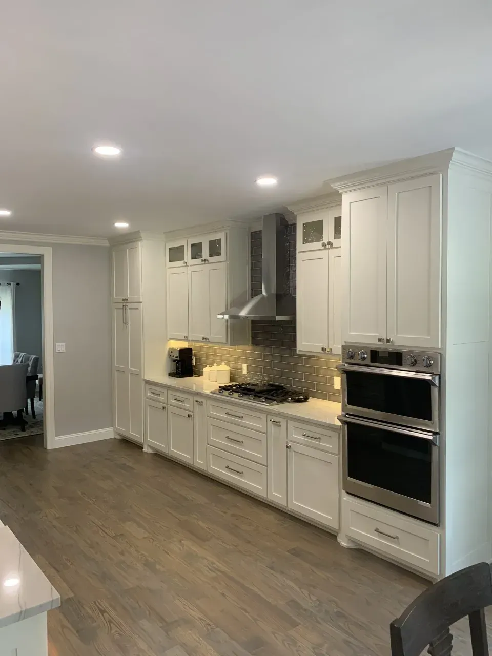 White kitchen with light wood flooring, cabinets, stainless steel appliances, and recessed lighting.