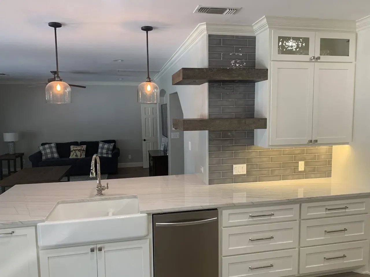 Modern kitchen with white cabinets, marble countertop, and open shelves against a brick backsplash.
