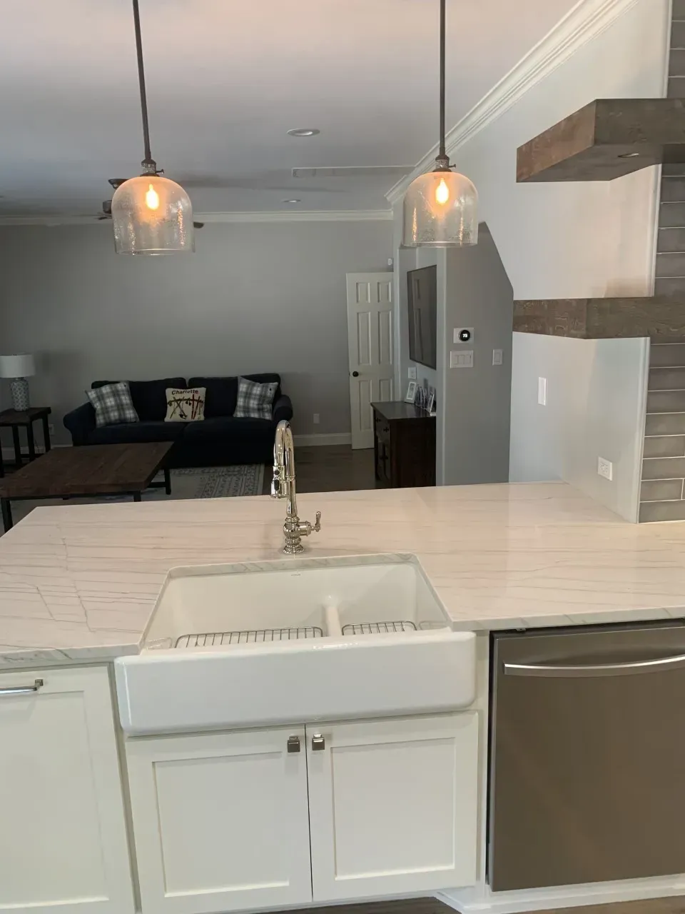 Kitchen with white cabinets, farmhouse sink, pendant lights, and view of living room with sofa.