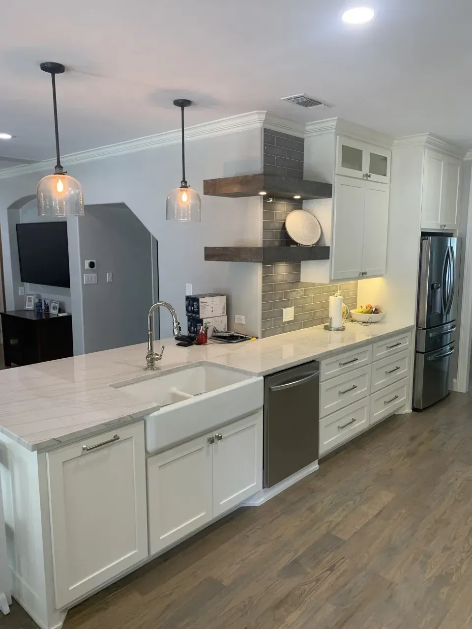 White kitchen with island, stainless steel appliances, marble countertop, pendant lights.