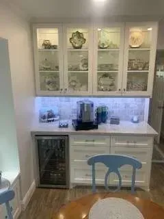 White built-in kitchen cabinet with glass-front display, countertop, and a mini-fridge.