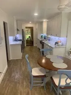 Kitchen with white cabinets, wooden floor, and a round dining table with chairs.
