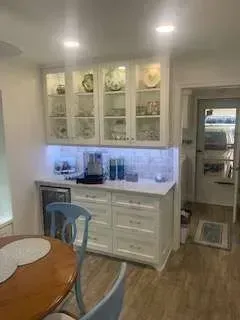 White kitchen cabinets with glass doors, illuminated countertop, and a wooden table.