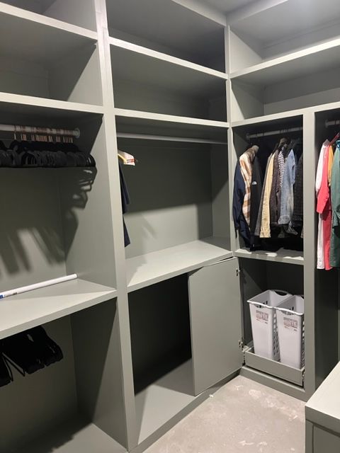A gray closet with shelves and hanging rods, some clothes, and a pull-out laundry hamper.