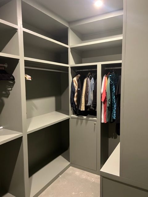 Walk-in closet with olive-green shelving and hanging rods. Some clothes hang; other shelves are empty.