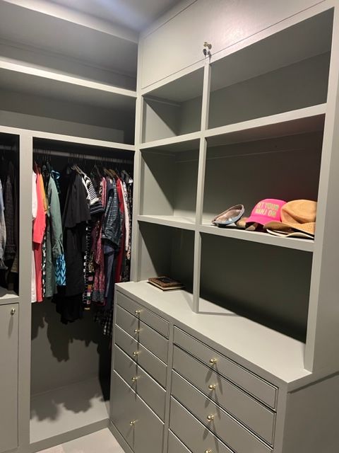 Gray walk-in closet with shelves, drawers, and hanging clothes. Hats on shelf.