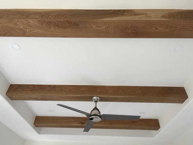 Ceiling with white surface and dark wood beams. A ceiling fan is installed.