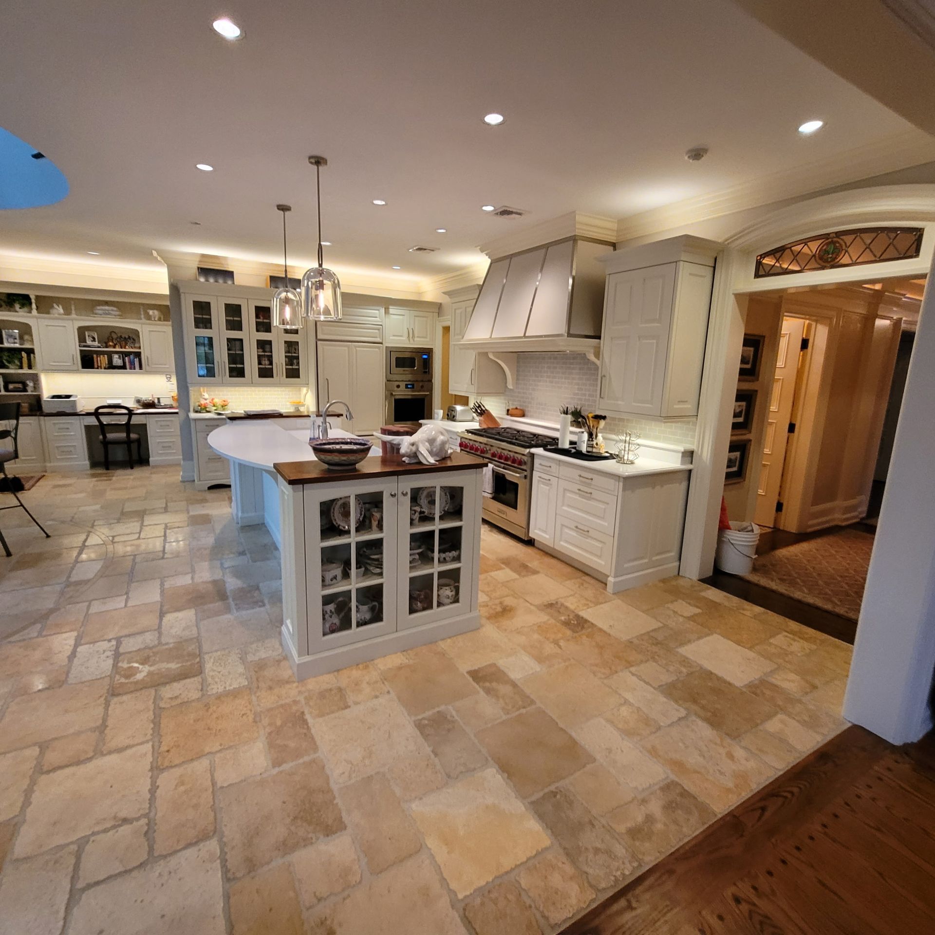 Spacious kitchen with a large island, light cabinetry, stone flooring, and a doorway to another room.