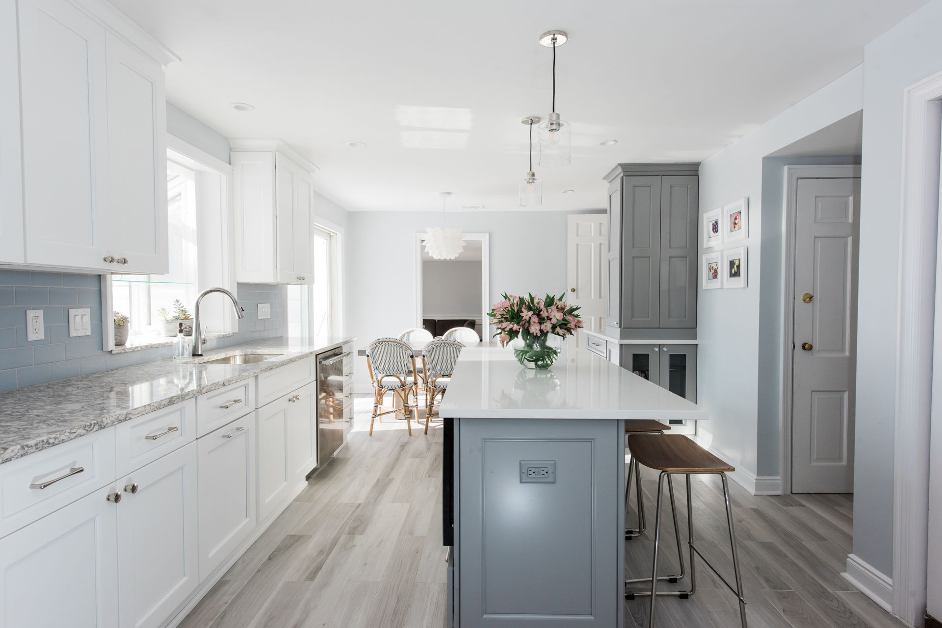 Modern white kitchen with gray island and light blue walls, leading to dining area.