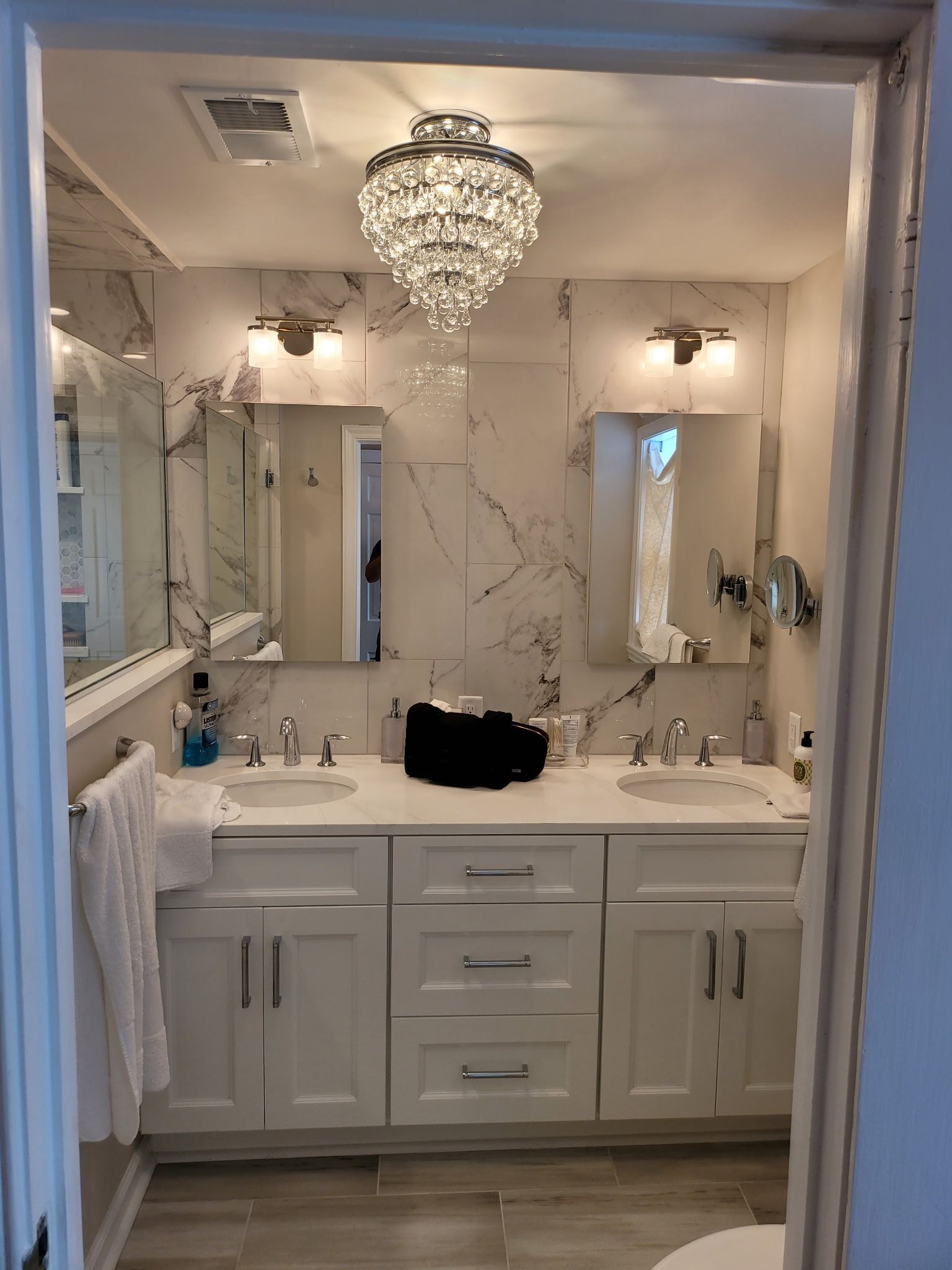A renovated bathroom with a white double vanity, mirrors, and a crystal chandelier.