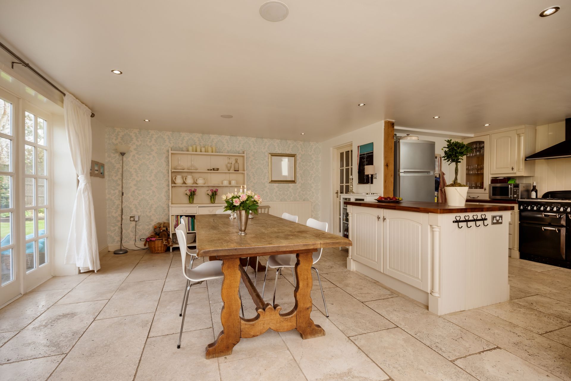 Spacious white kitchen with large wooden dining table, white cabinets, stainless steel appliances, and French doors. Spacious white kitchen with large wooden dining table, white cabinets, stainless steel appliances, and French doors.