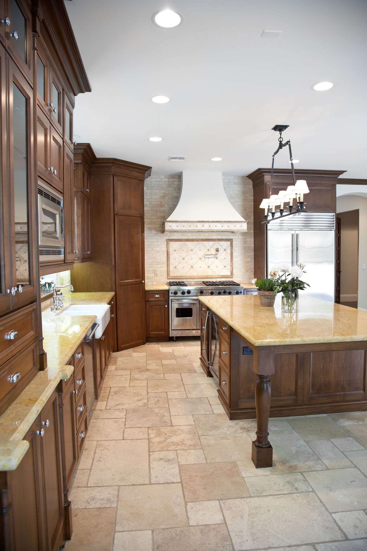 Kitchen with wood cabinets, tile floor, large island with granite countertop, and white range hood. Kitchen with wood cabinets, tile floor, large island with granite countertop, and white range hood.