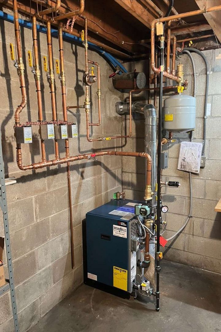 A boiler is sitting in a basement surrounded by pipes.