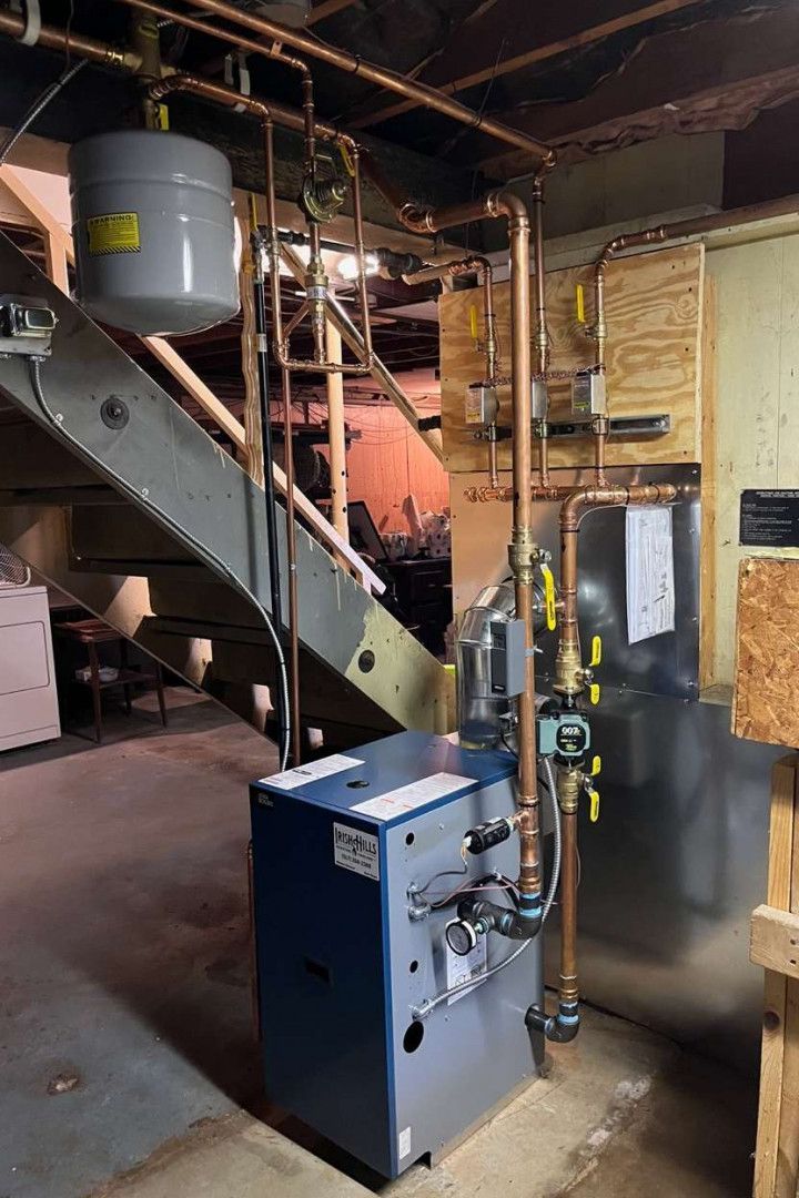 A blue boiler is sitting in a basement next to a staircase.