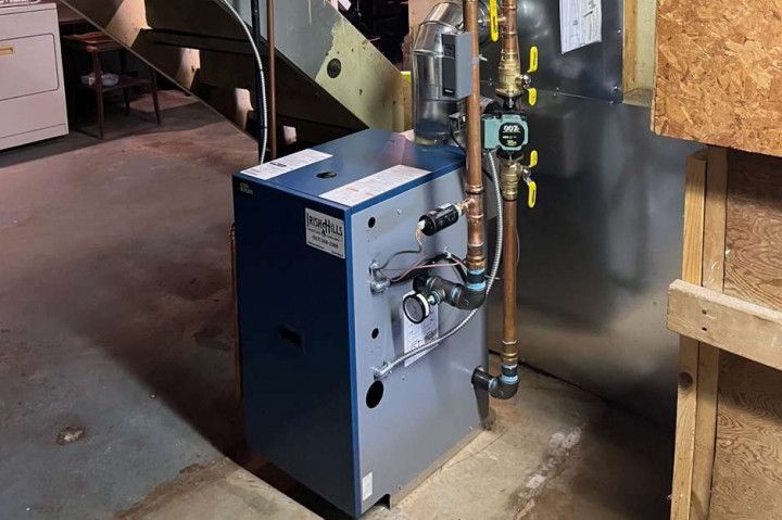 A blue boiler is sitting in a basement next to a staircase.