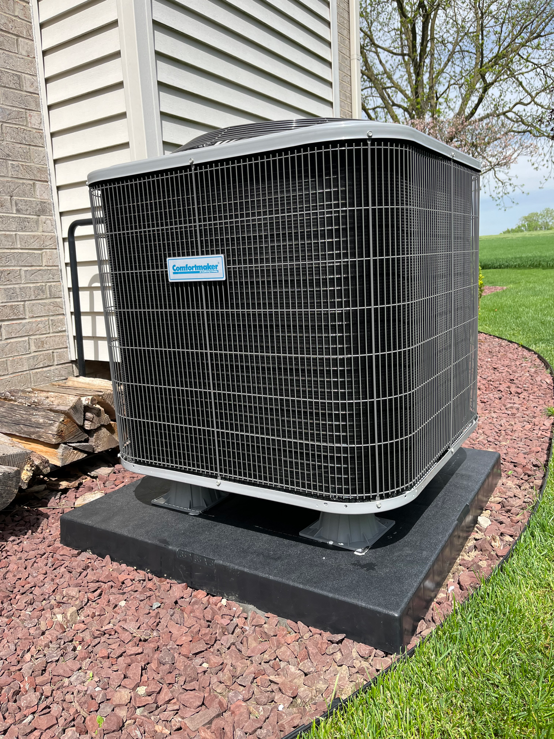 An air conditioner is sitting outside of a house on a black base.