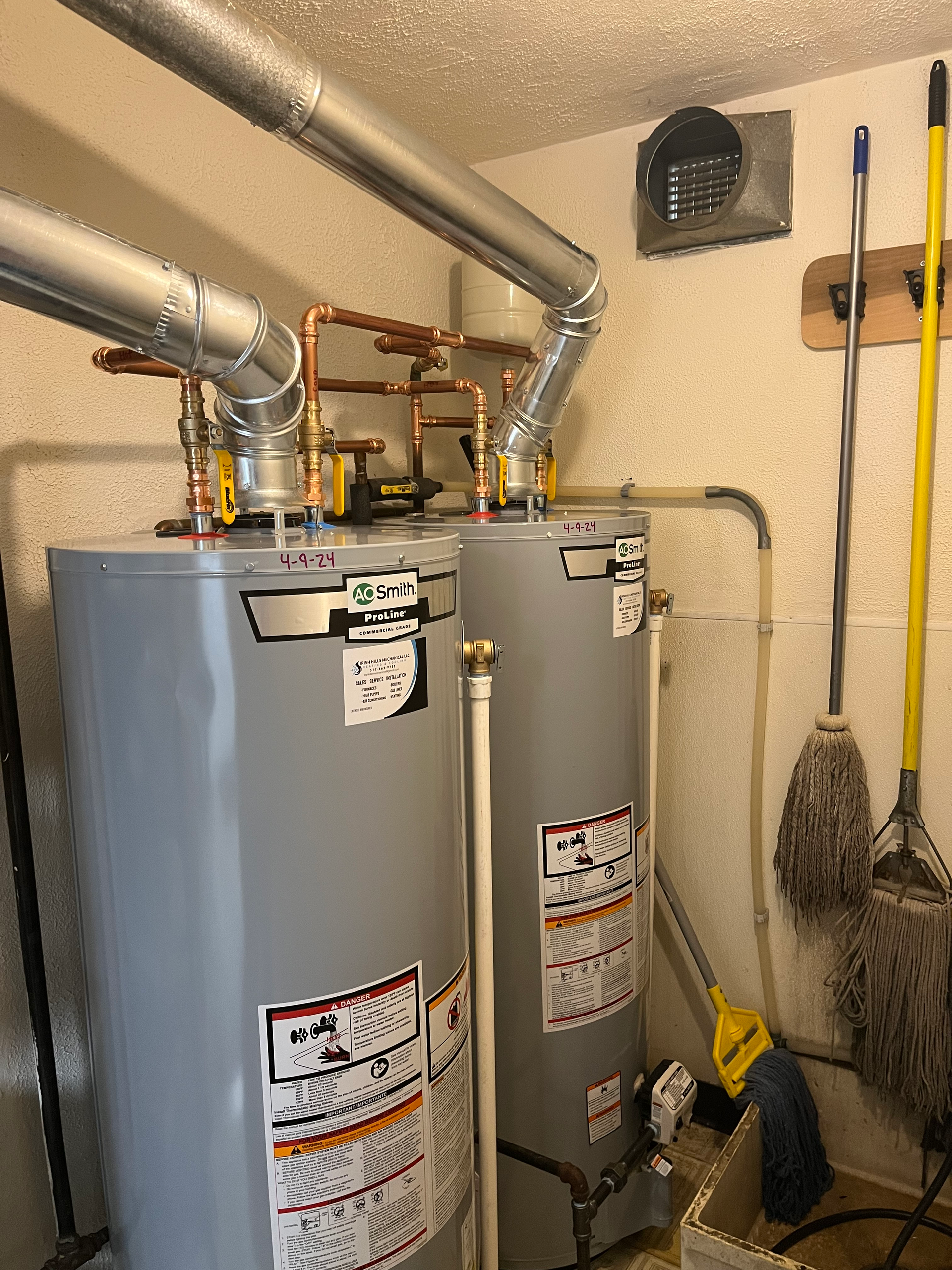 A white water heater is hanging on a wall next to copper pipes.