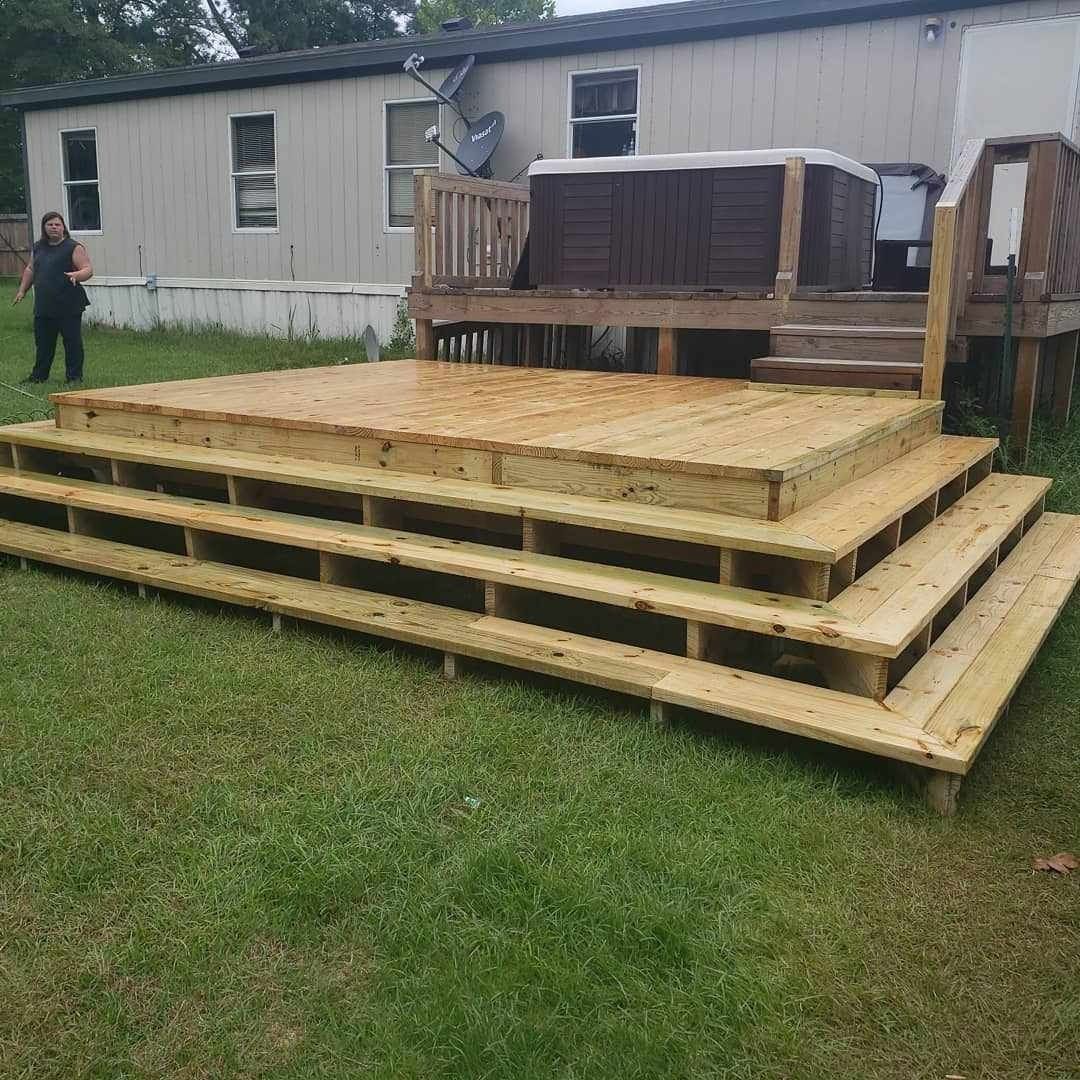 A wooden deck with stairs and a hot tub in front of a mobile home.