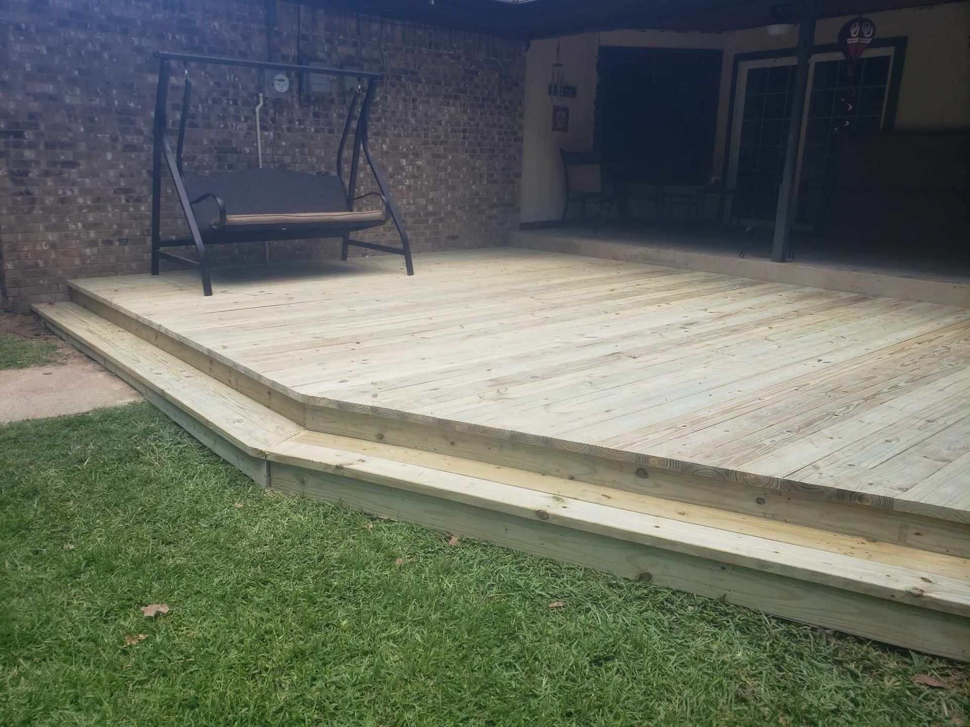 A wooden deck with a swing on it in a backyard.
