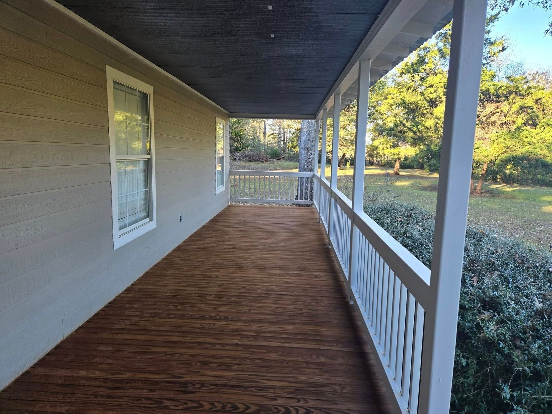 The porch of a house with a wooden deck and a white railing.