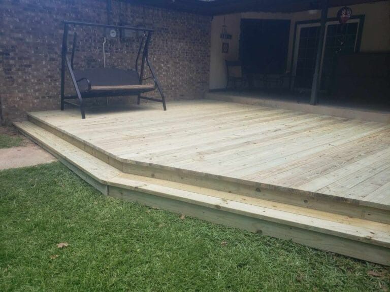 A wooden deck with a swing on it in a backyard.