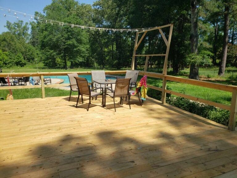 A wooden deck with a table and chairs and a pool in the background.