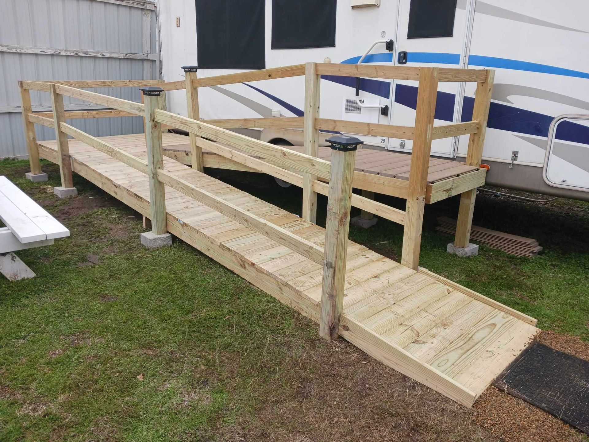 A wooden ramp is attached to a rv in the grass.