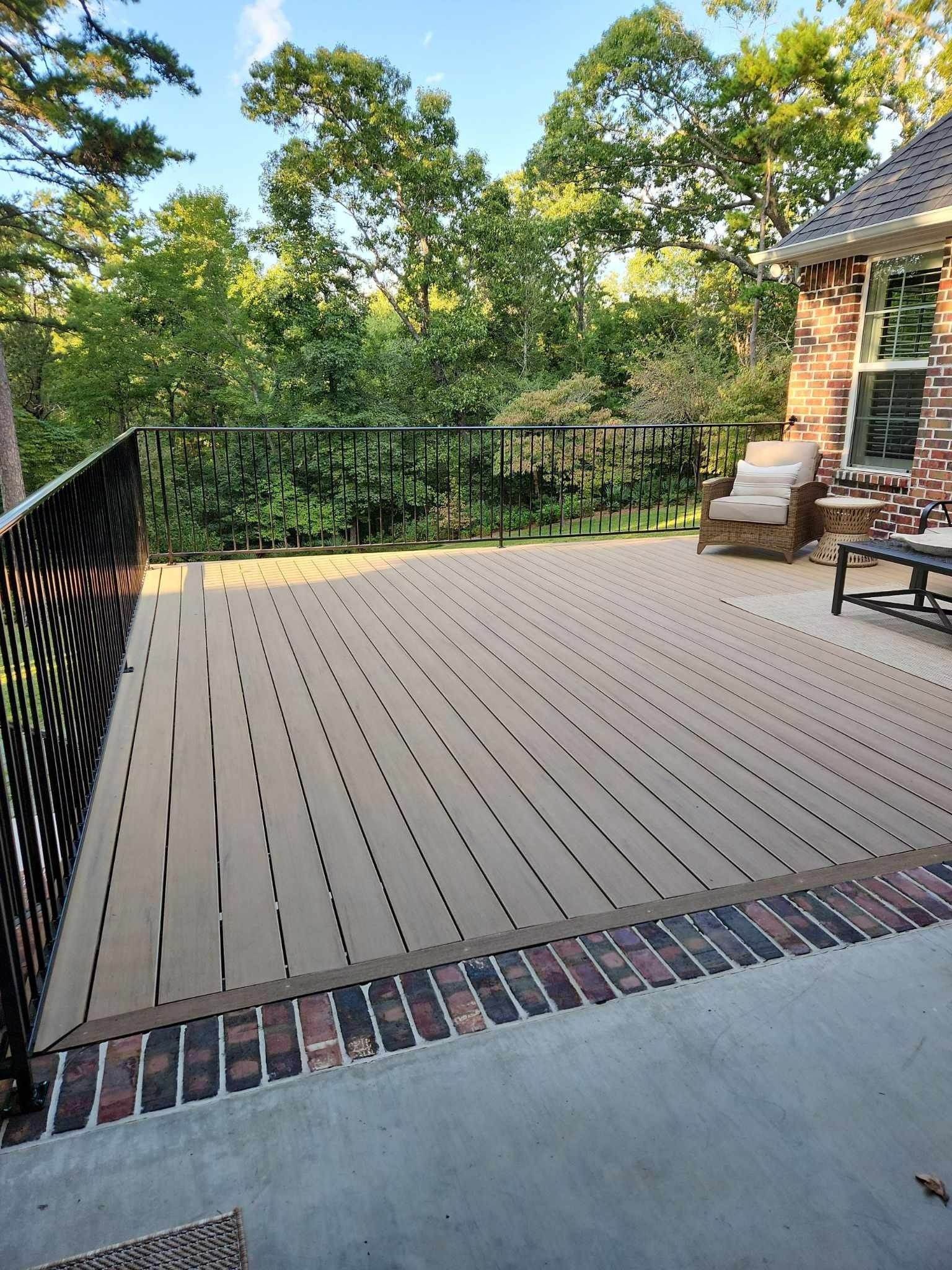 A large deck with a railing and a view of trees and a house.