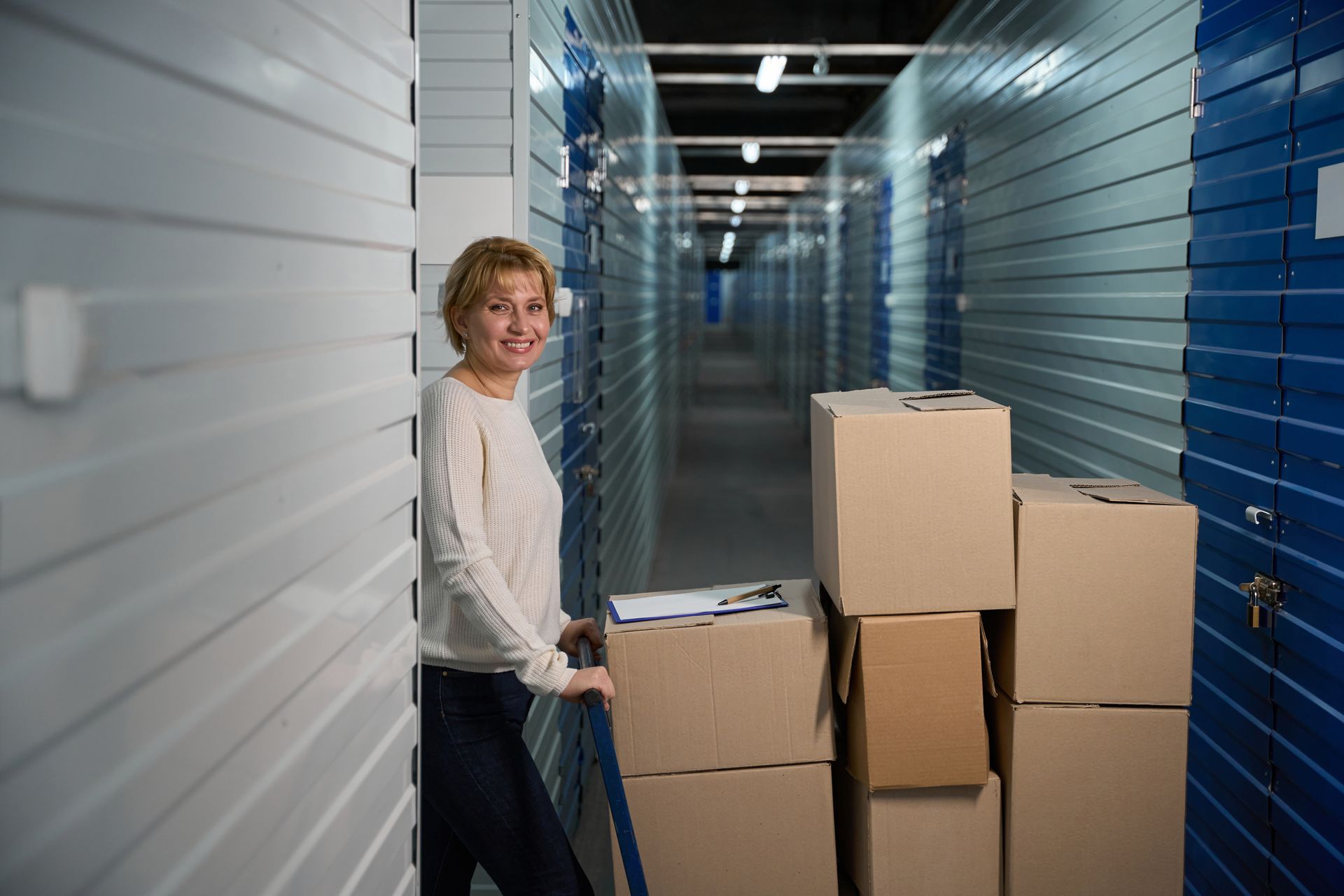 Woman standing in a storage facility hallway next to stacked moving boxes