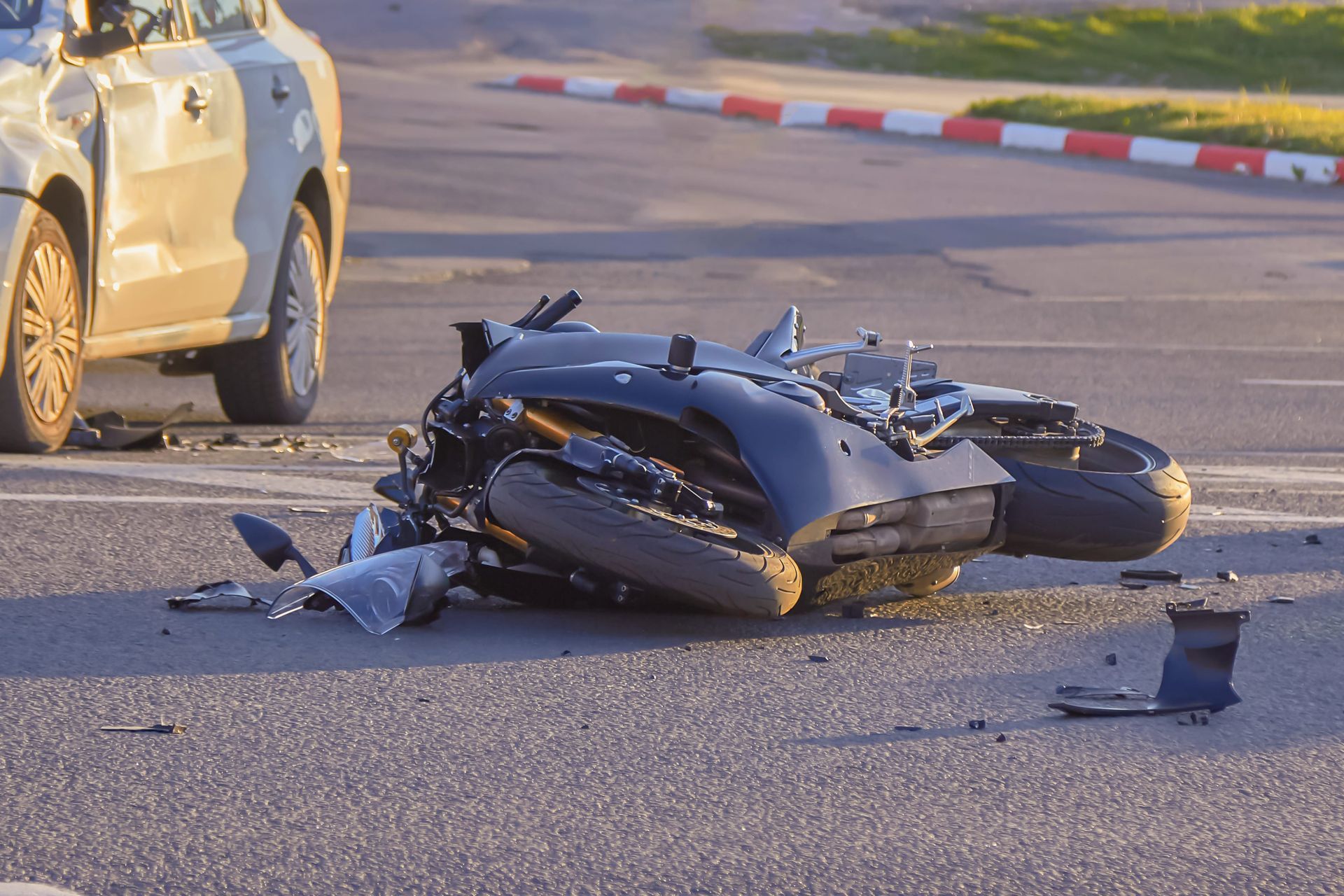 A wrecked black motorcycle lies on its side on an asphalt road next to a damaged car.