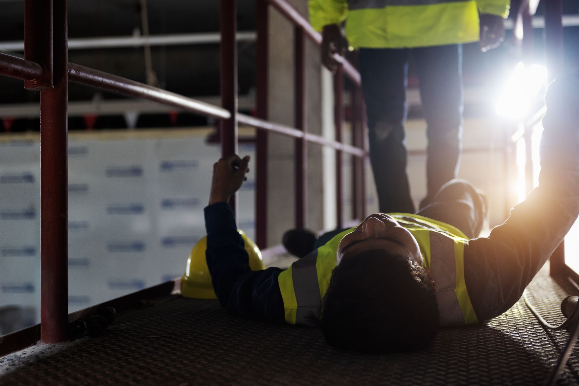 Construction worker lying on a platform after falling. Another worker stands nearby.