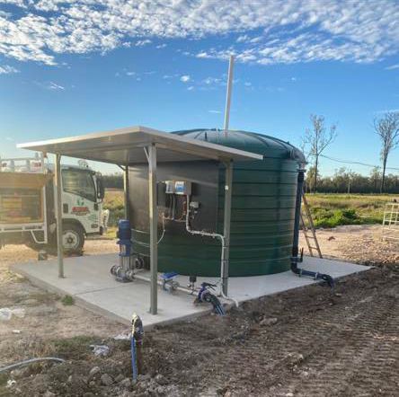 A green water tank is sitting in the middle of a dirt field next to a truck.