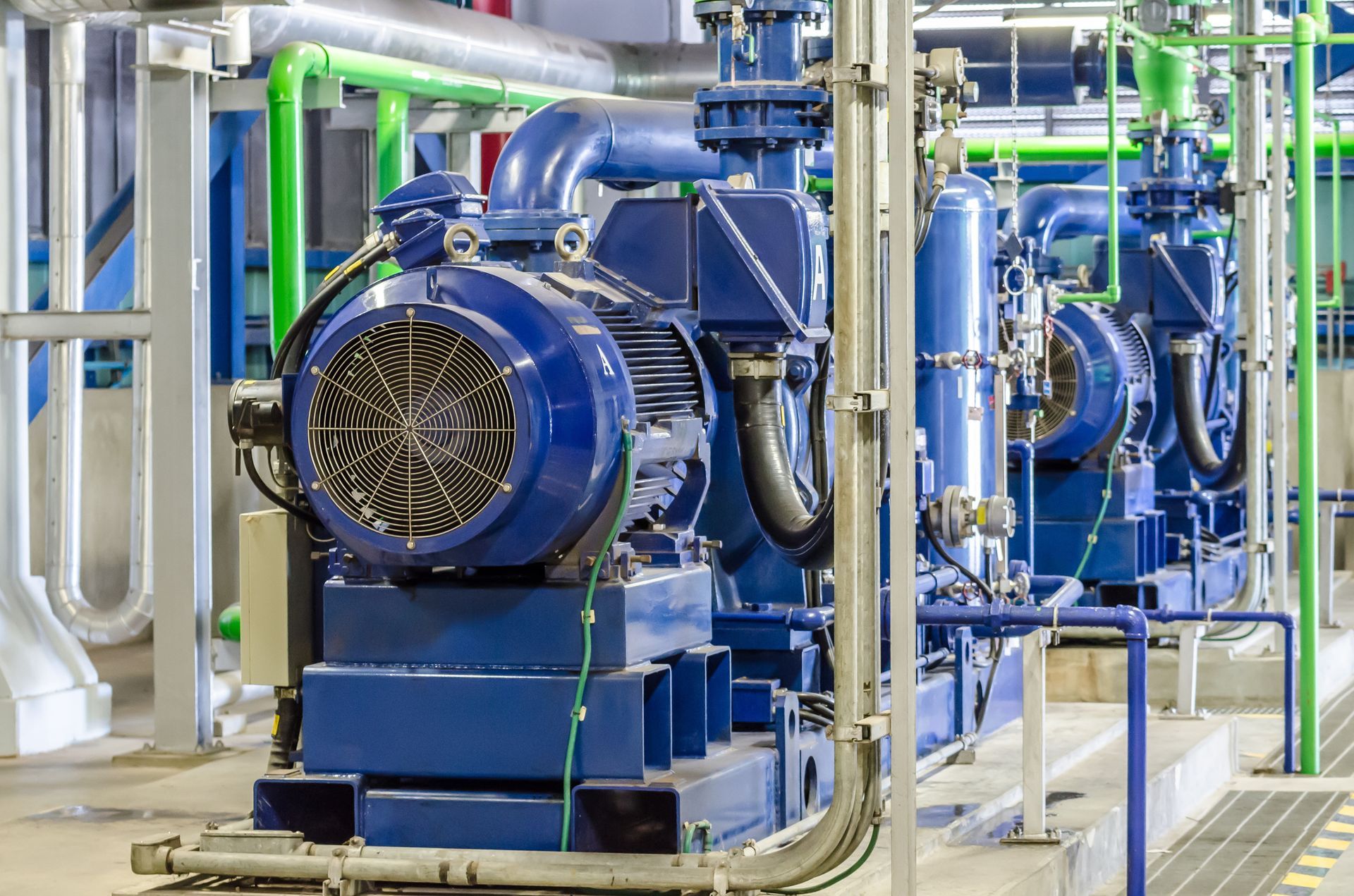 A row of blue pumps and pipes in a factory.