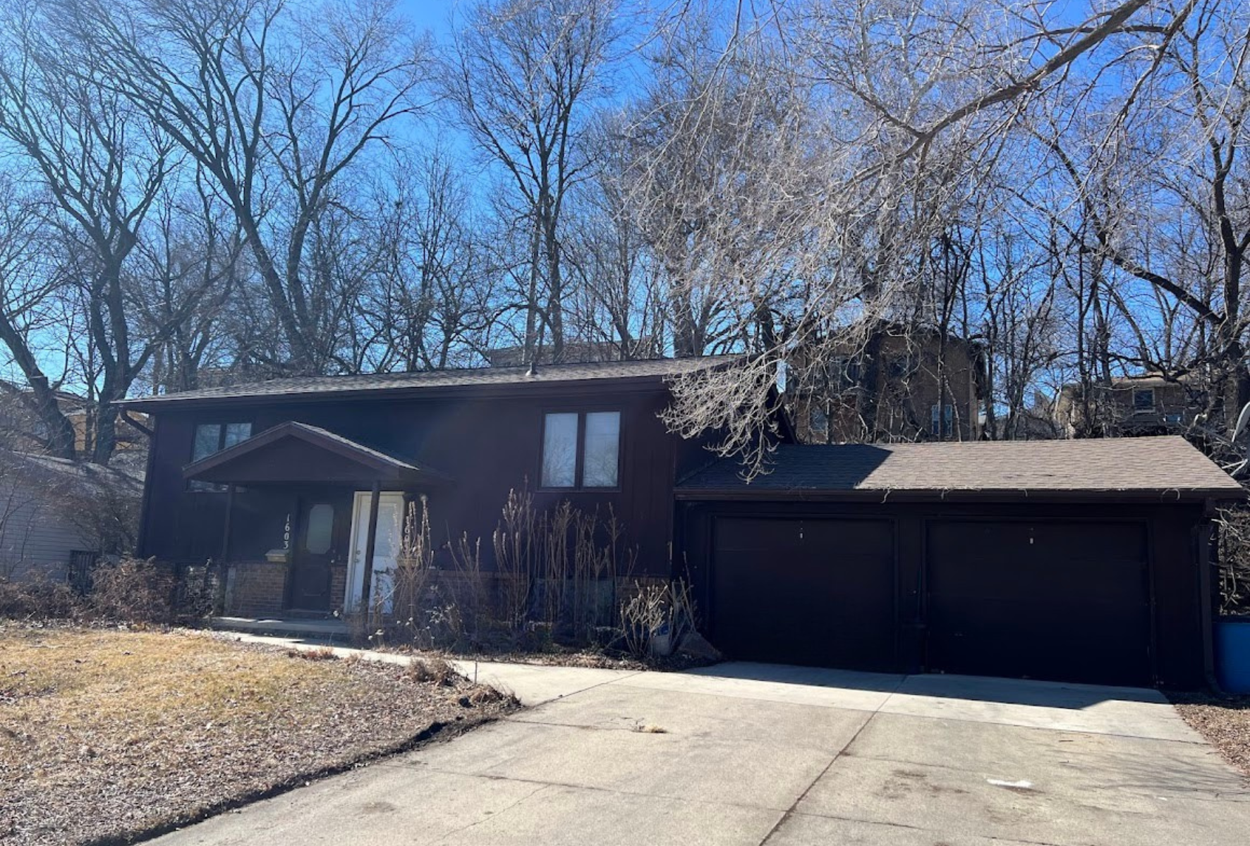 A large brown house with a garage and trees in the background.
