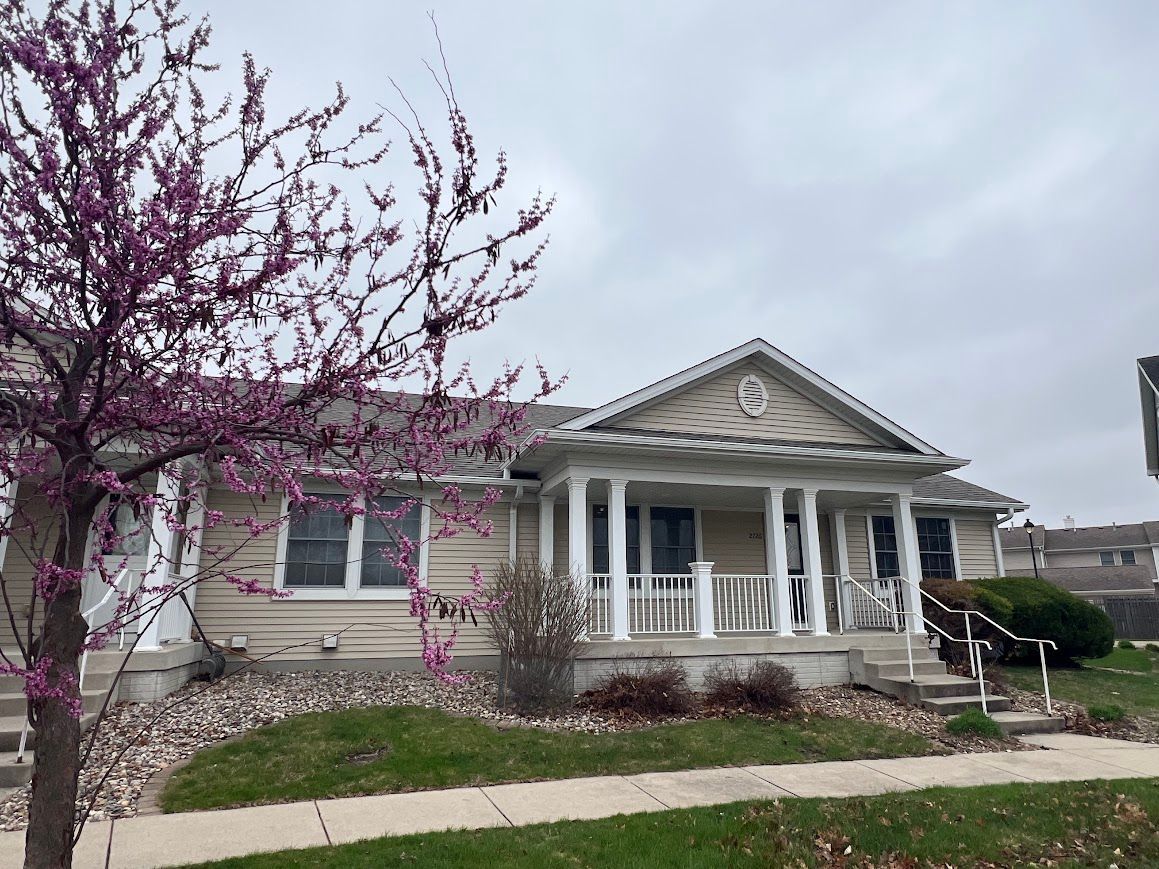A house with a porch and a tree in front of it.