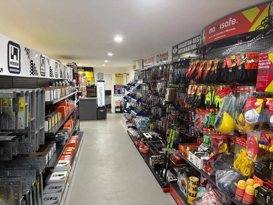 Inside view of a hardware store aisle, shelves stocked with various tools, gloves, and safety equipment.