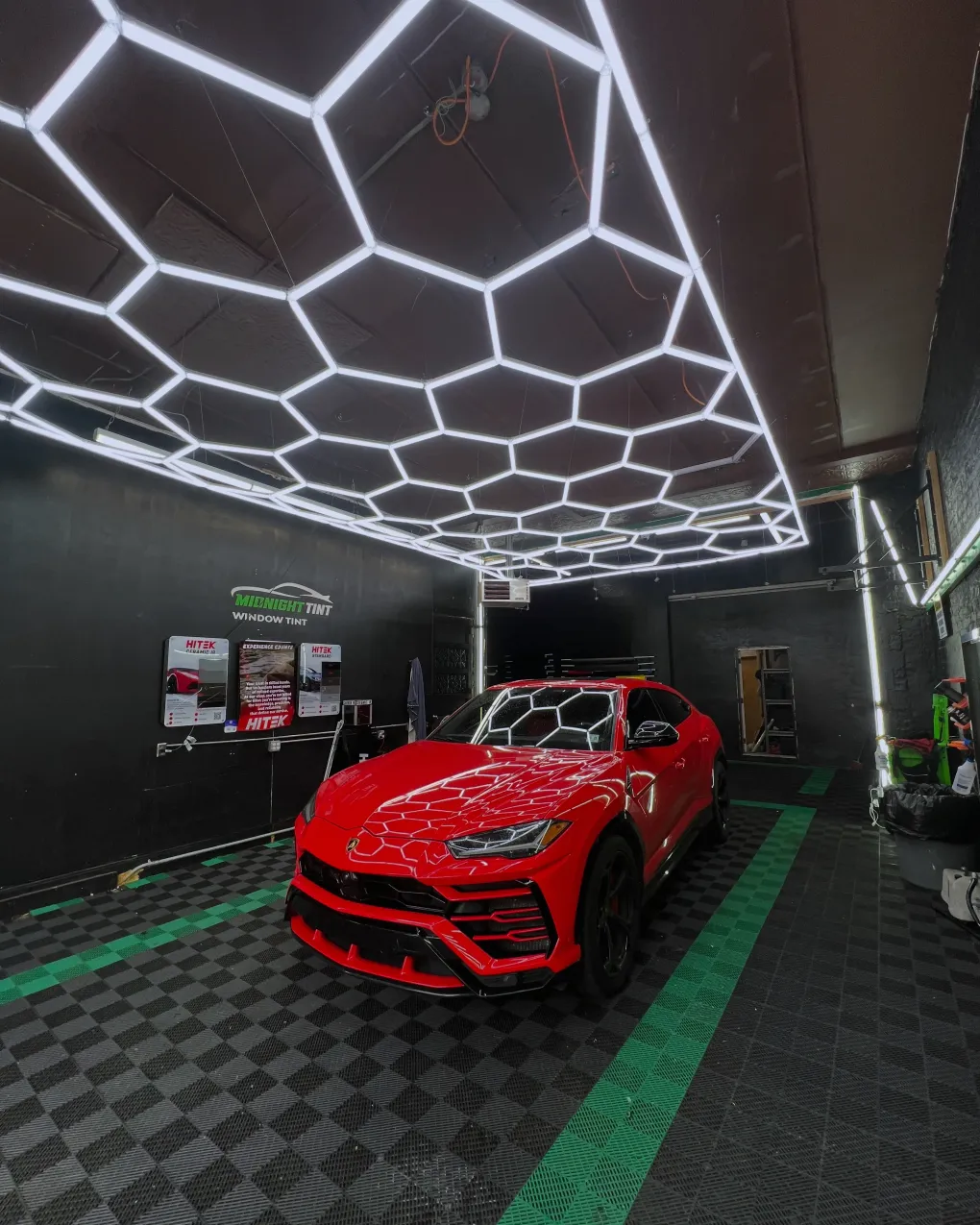 Red Lamborghini in a car detailing studio with honeycomb ceiling lights.
