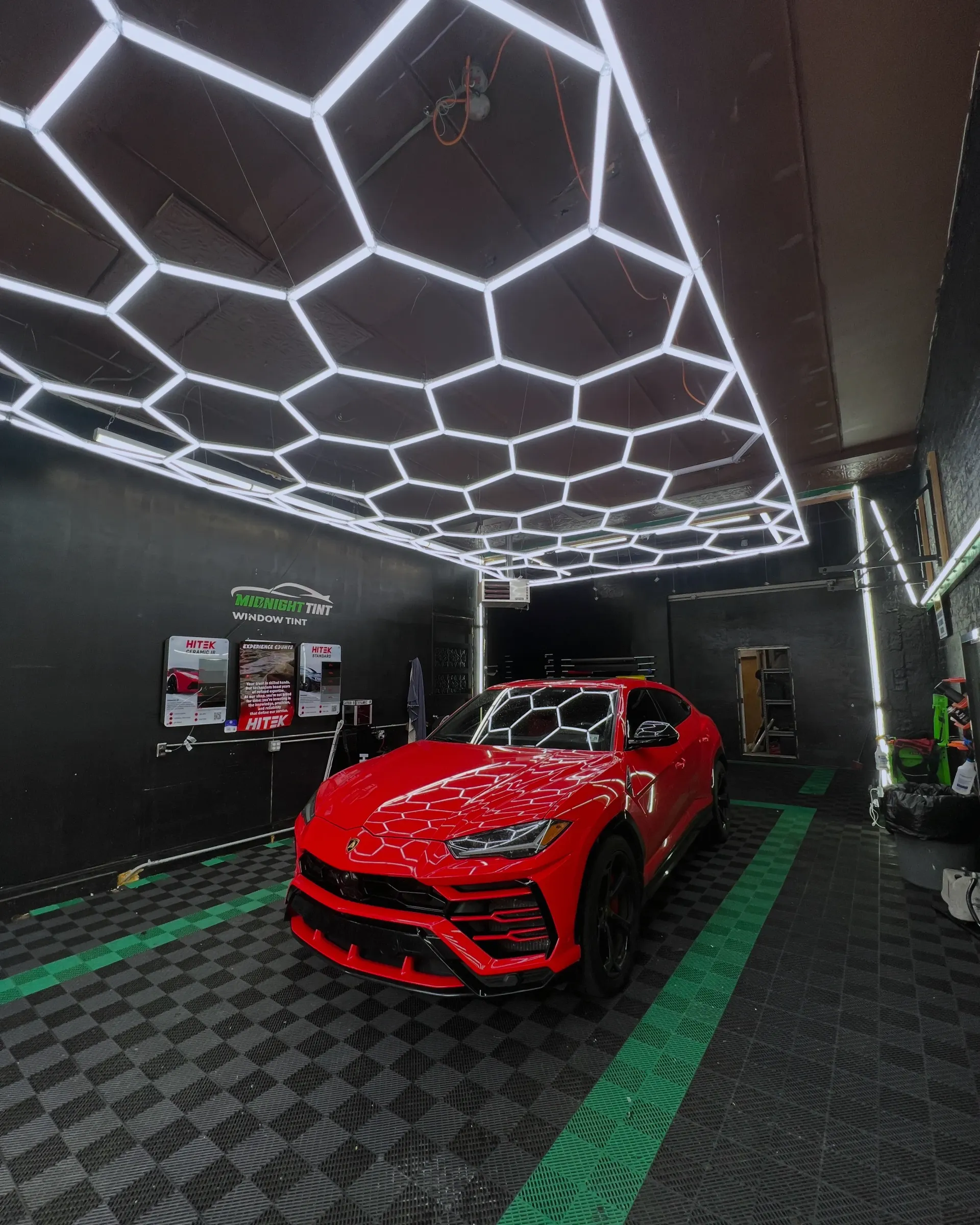 Red Lamborghini in a car detailing studio with honeycomb ceiling lights.