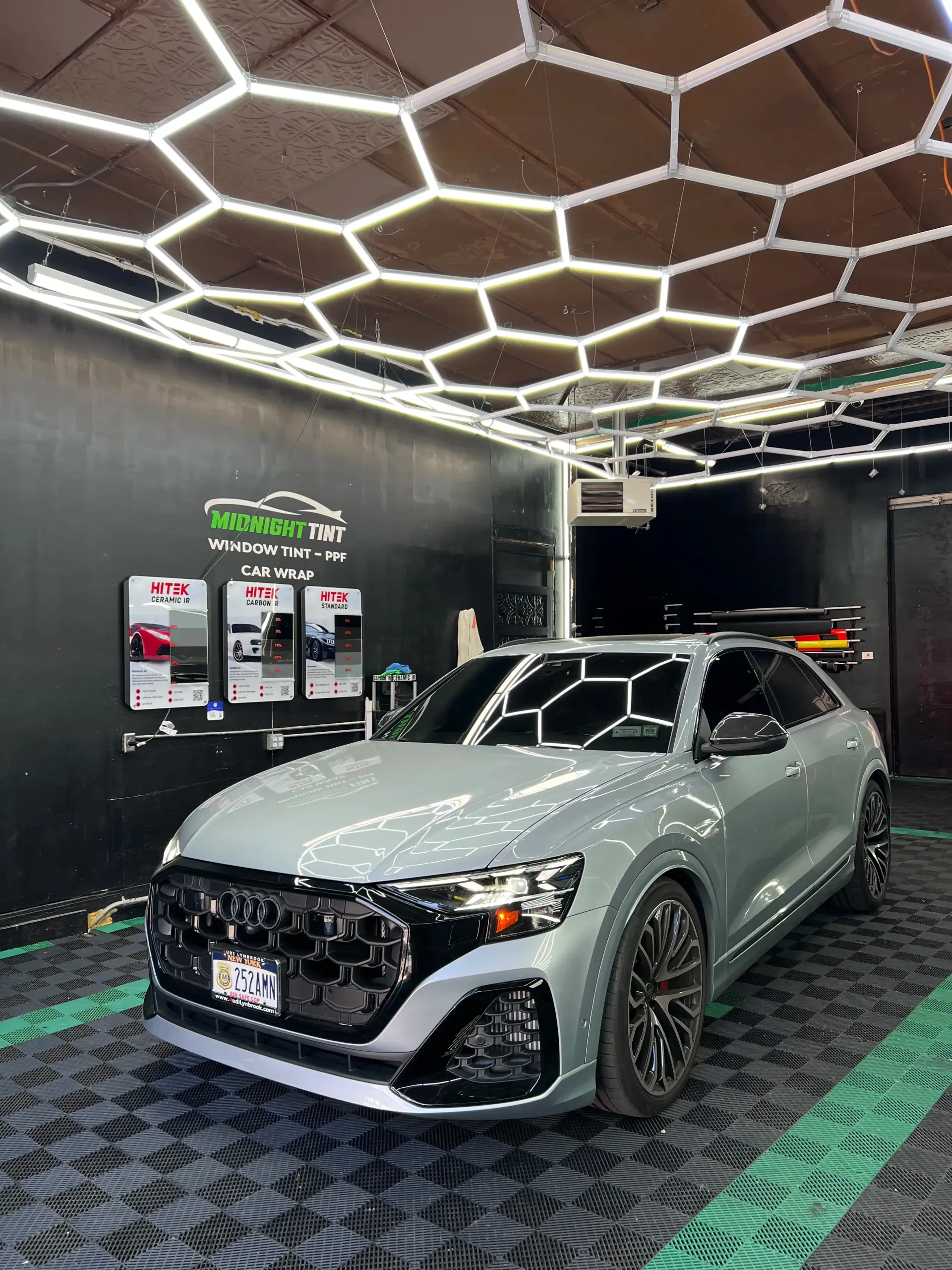 Gray Audi SUV inside a shop with hexagonal lights. Black grill, wheels, and tinted windows.