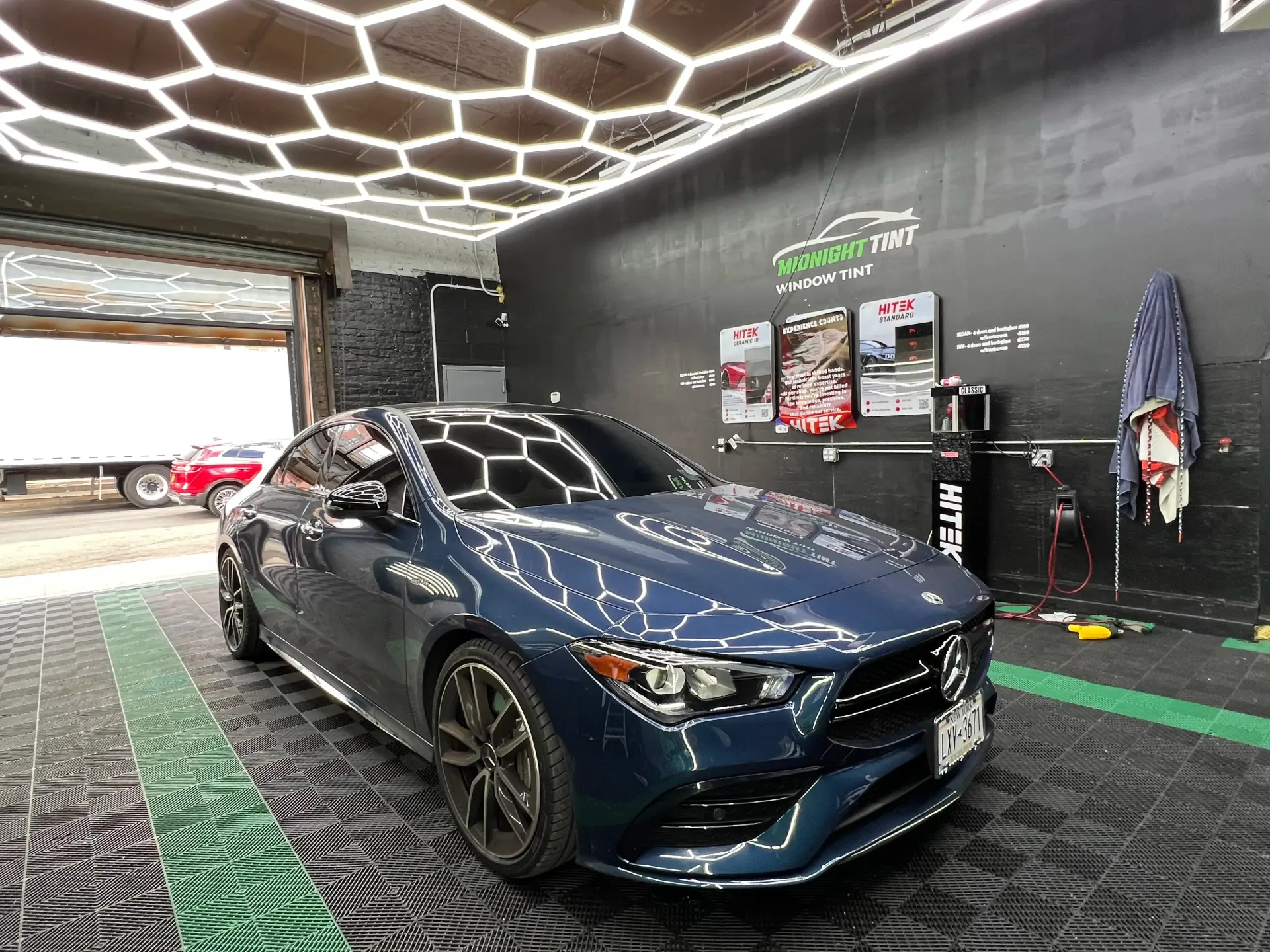 Blue Mercedes CLA sedan parked in a car detailing shop with hexagonal ceiling lights.