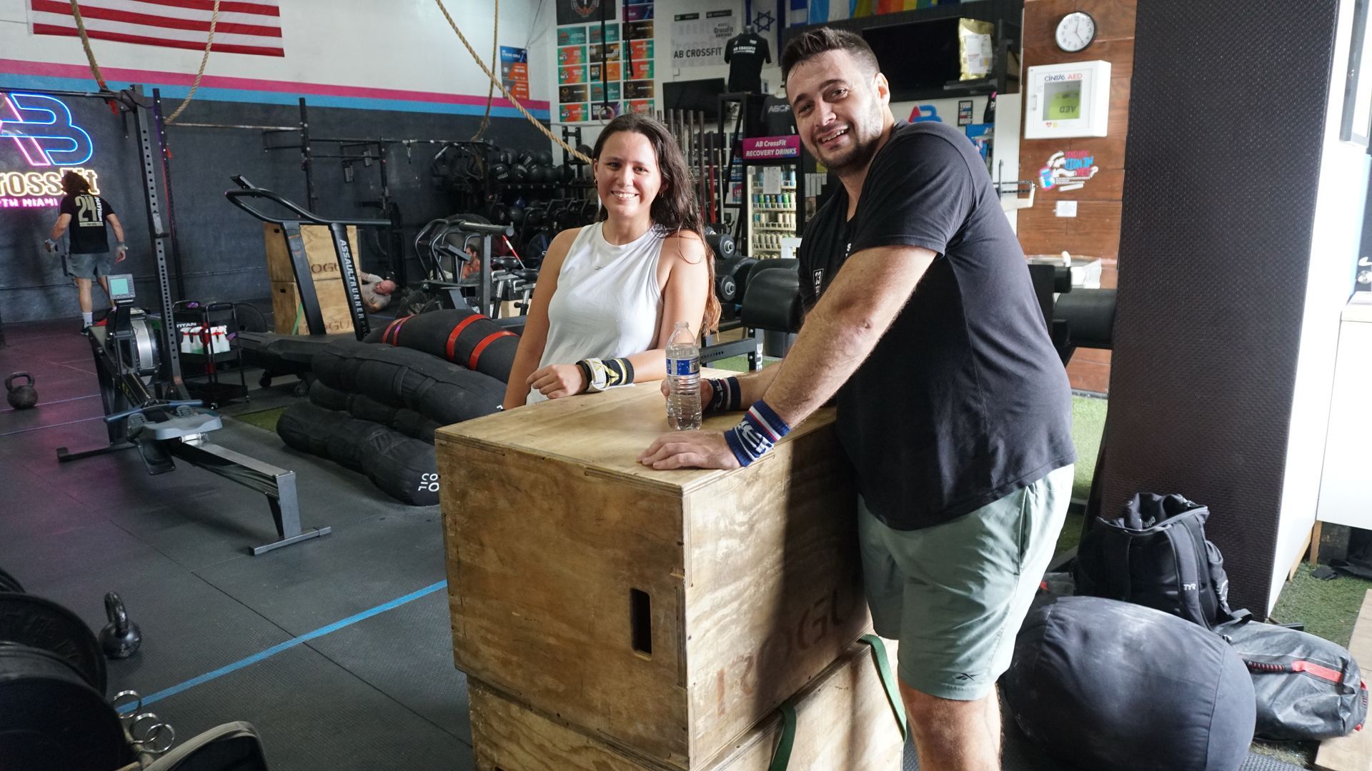 A man and a woman are standing next to a wooden box in a gym.