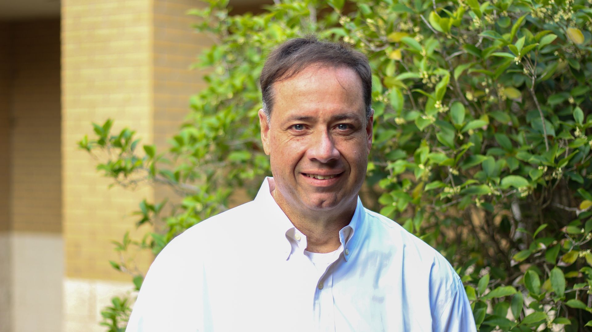 A man in a gray shirt is smiling in front of a church.