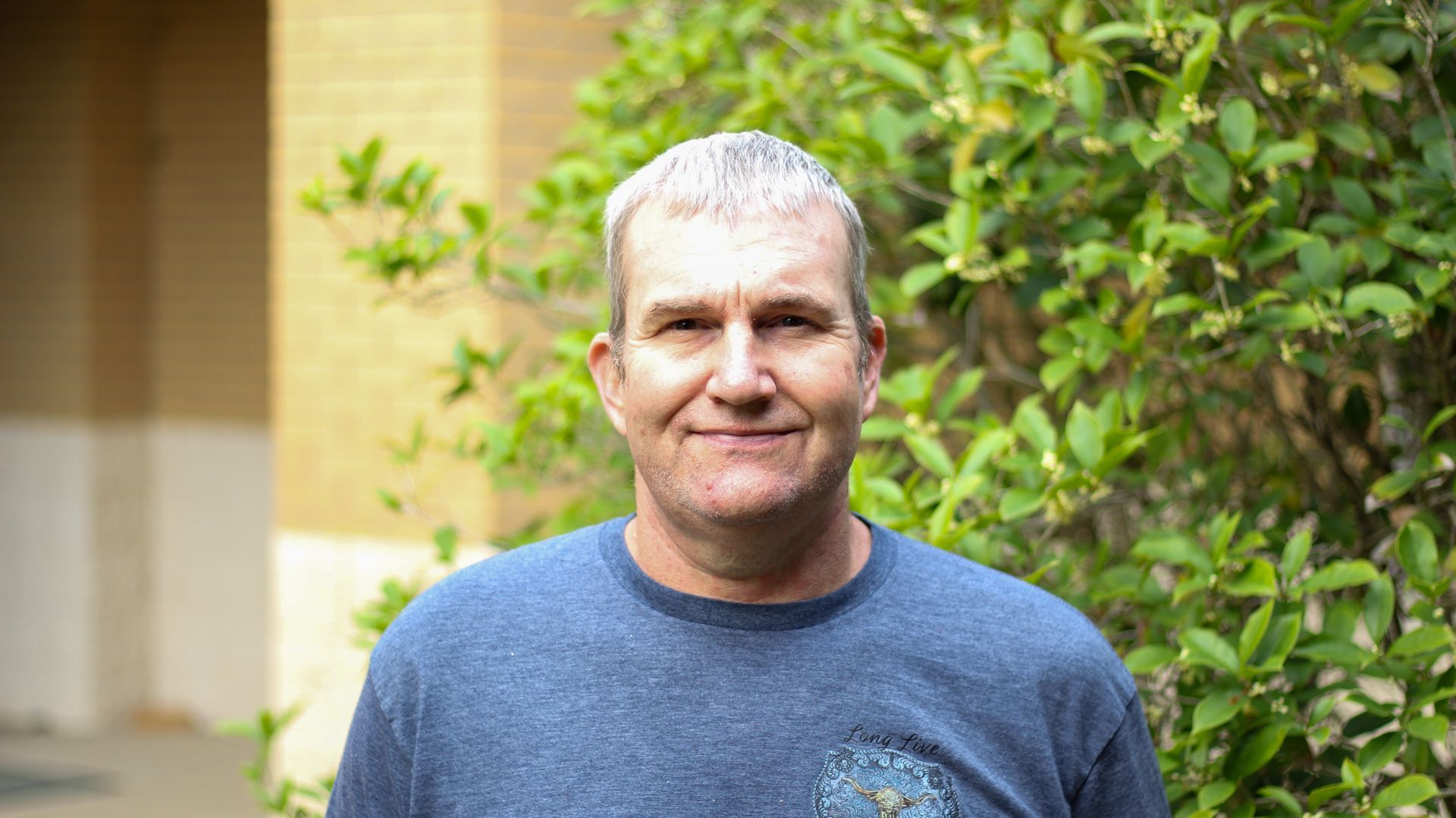 A woman is smiling in front of a church filled with wooden benches.