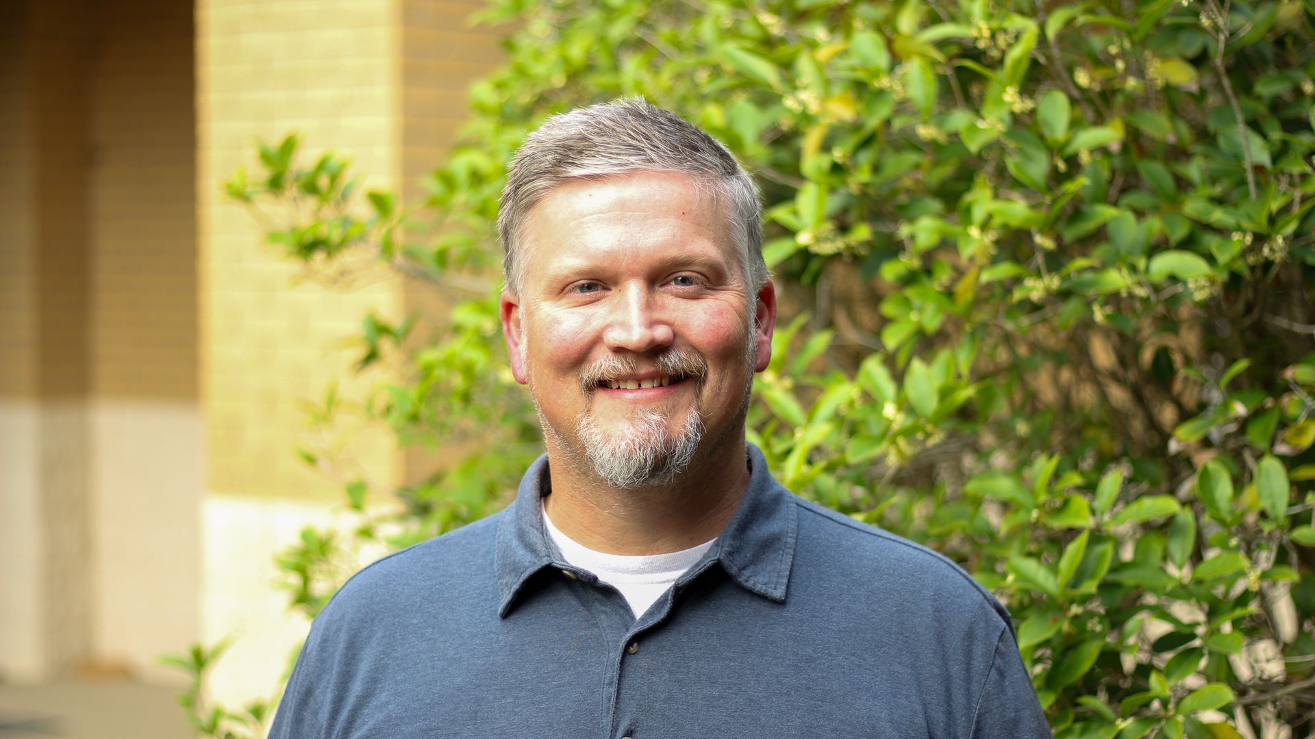 A man with a beard is smiling for the camera in front of a church.
