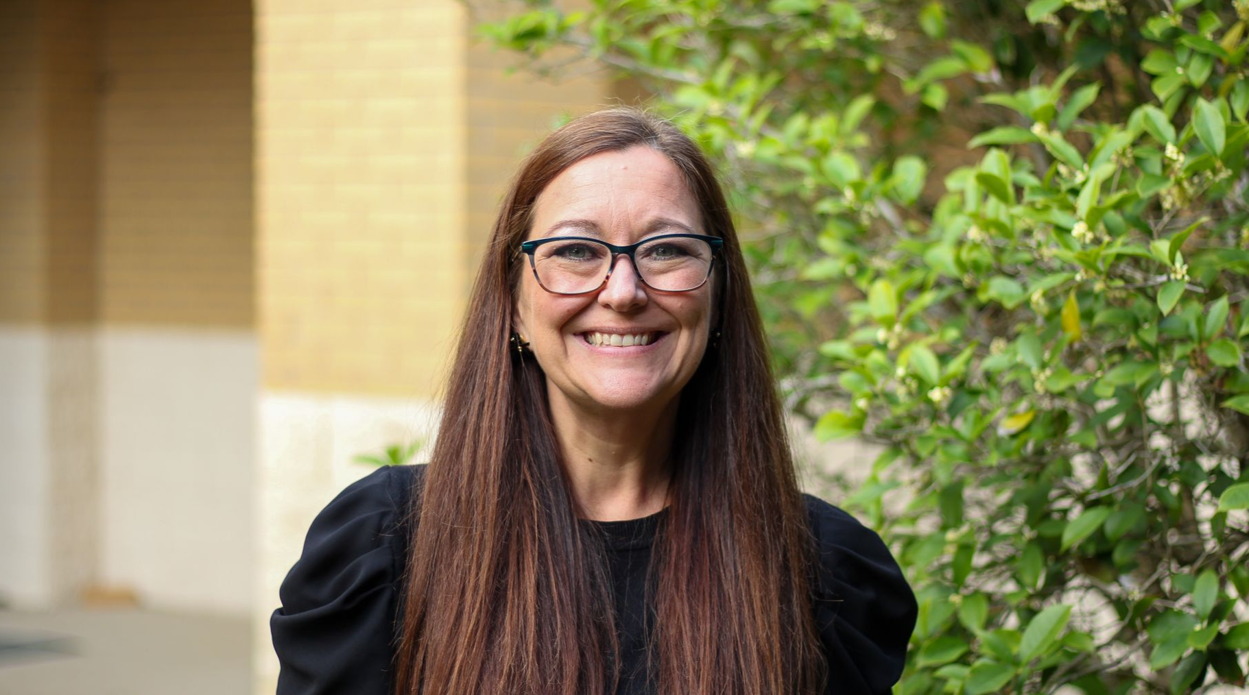 A woman is smiling in front of a church filled with wooden benches.
